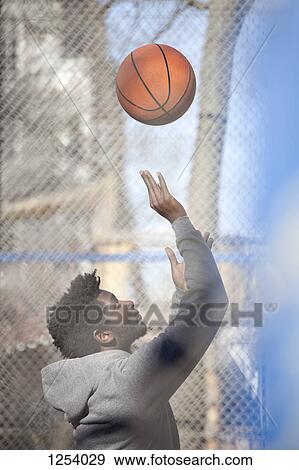 Stock Photo - A hip young man playing basketball on a public outdoor court. Fotosearch