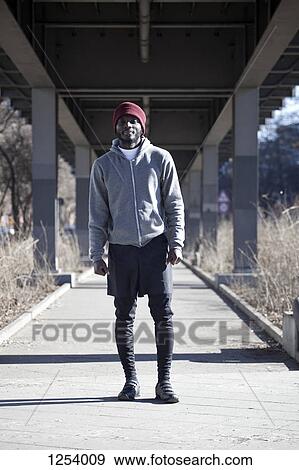 Stock Photo - A hip young man standing in sports gear on a footpath under a bridge. Fotosearch