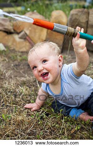 Stock Image - A laughing baby boy holding a garden hose. Fotosearch