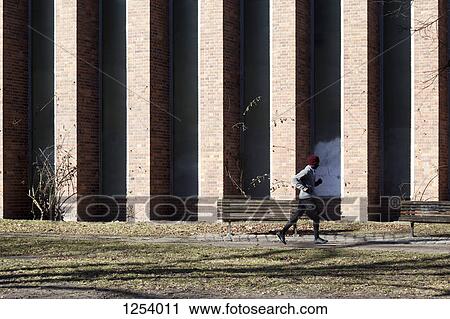 Stock Image - A man jogging along a sidewalk in the city during springtime. Fotosearch