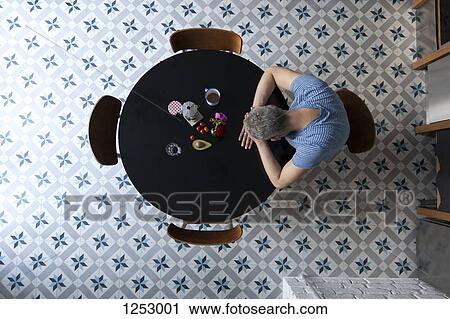 A man sitting at a table with his head resting on his arms, directly above View Large Photo Image Stock Image - A man sitting at a table with his head resting on his arms, directly above. Fotosearch