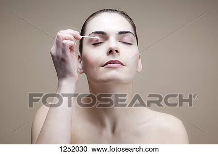 Stock Image - A serene young woman using a cotton swab on her eye. Fotosearch