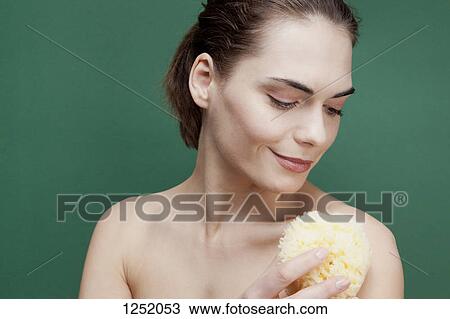 Stock Image - A serenely smiling woman using a bath sponge on her shoulder. Fotosearch