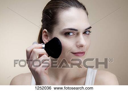 A serenely smiling young woman applying blush with a make-up brush View Large Photo Image Stock Photograph - A serenely smiling young woman applying blush with a make-up brush. Fotosearch