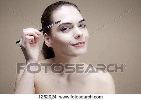 A serenely smiling young woman brushing her eyebrow with a brow brush View Large Photo Image Picture - A serenely smiling young woman brushing her eyebrow with a brow brush. Fotosearch