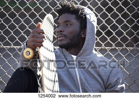 A serious young man leaning against a chain link fence holding a skateboard View Large Photo Image Stock Image - A serious young man leaning against a chain link fence holding a skateboard. Fotosearch