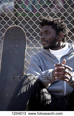 A serious young man leaning against a chain link fence next to a skateboard View Large Photo Image Stock Image - A serious young man leaning against a chain link fence next to a skateboard. Fotosearch