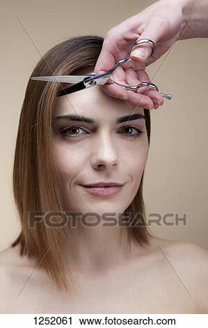 Stock Image - A smiling woman getting her hair cut by a hand holding scissors. Fotosearch