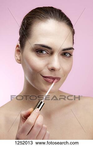 A smiling young woman applying lip gloss View Large Photo Image Stock Image - A smiling young woman applying lip gloss. Fotosearch