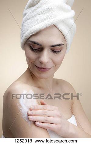 A smiling young woman applying lotion to her skin View Large Photo Image Stock Photo - A smiling young woman applying lotion to her skin. Fotosearch