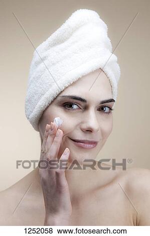 A smiling young woman applying moisturizer to her cheek View Large Photo Image Stock Photo - A smiling young woman applying moisturizer to her cheek. Fotosearch