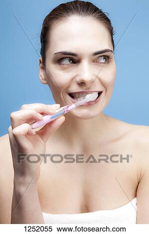 Stock Photography - A smiling young woman brushing her teeth while looking away contemplatively. Fotosearch