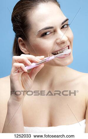 Stock Image - A smiling young woman brushing her teeth. Fotosearch