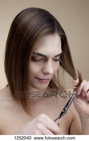 Stock Image - A smiling young woman concentrating while cutting her own hair. Fotosearch