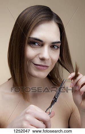 A smiling young woman cutting her own hair View Large Photo Image Stock Photo - A smiling young woman cutting her own hair. Fotosearch