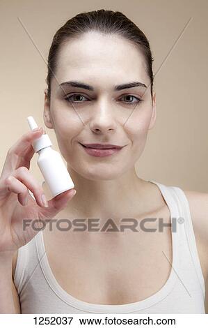 Stock Photo - A smiling young woman holding a bottle of nasal spray. Fotosearch