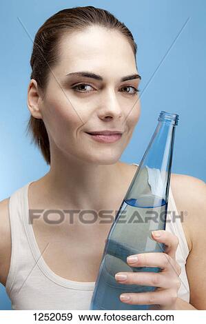 Stock Photo - A smiling young woman holding a glass bottle of water. Fotosearch