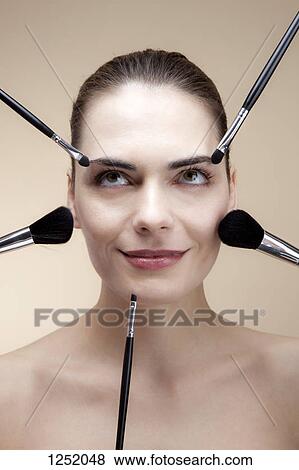 Stock Photo - A smiling young woman looking up with various make-up brushes around her face. Fotosearch