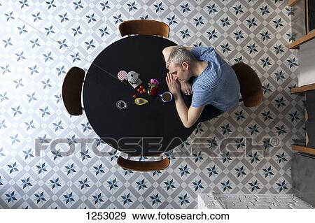 Stock Photo - A tired man with his head resting on his arms sitting at a table, directly above. Fotosearch