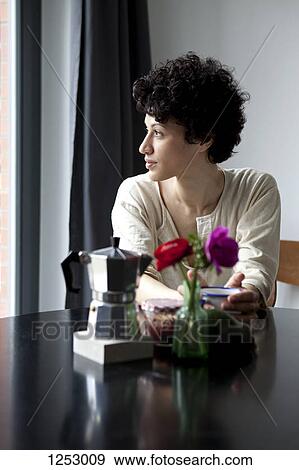 A woman sitting at a table looking thoughtfully out of a window View Large Photo Image Stock Photo - A woman sitting at a table looking thoughtfully out of a window. Fotosearch