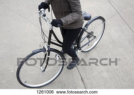 Stock Photograph - A woman standing with her bicycle on a sidewalk. Fotosearch