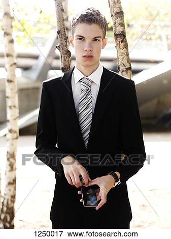 A young businessman holding a smart phone and looking serious View Large Photo Image Stock Photo - A young businessman holding a smart phone and looking serious. Fotosearch
