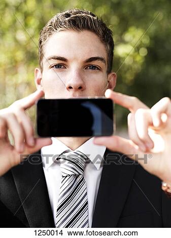 A young businessman holding his smart phone up in front of his mouth View Large Photo Image Picture - A young businessman holding his smart phone up in front of his mouth. Fotosearch