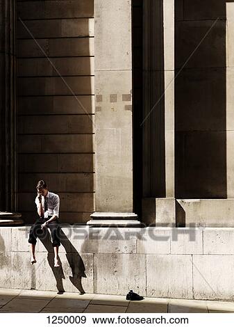 A young businessman sitting outside with his shoes kicked off using a mobile phone View Large Photo Image Stock Photo - A young businessman sitting outside with his shoes kicked off using a mobile phone. Fotosearch