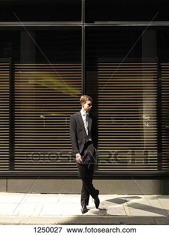 A young businessman standing outside a building, looking away View Large Photo Image Stock Photo - A young businessman standing outside a building, looking away. Fotosearch