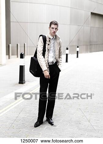 A young businessman with a laptop bag standing on a cobblestone sidewalk View Large Photo Image Stock Photo - A young businessman with a laptop bag standing on a cobblestone sidewalk. Fotosearch