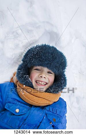 A young cheerful boy wearing warm clothing outdoors lying in the snow View Large Photo Image Picture - A young cheerful boy wearing warm clothing outdoors lying in the snow. Fotosearch