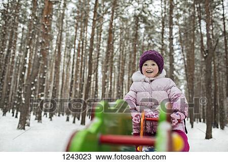Stock Image - A young cheerful girl on a piece of playground equipment in winter. Fotosearch
