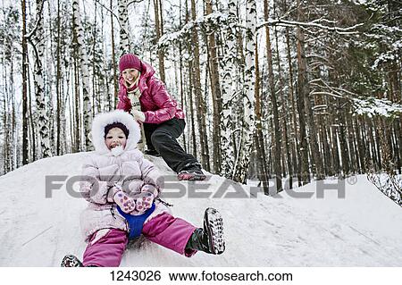 A young girl sledding while her mother looks on View Large Photo Image Stock Photograph - A young girl sledding while her mother looks on. Fotosearch