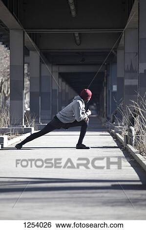 A young man doing a stretching lunge on a sidewalk under a bridge View Large Photo Image Stock Photograph - A young man doing a stretching lunge on a sidewalk under a bridge. Fotosearch