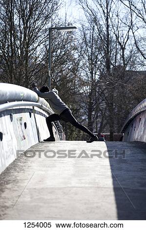 Stock Photography - A young man doing a stretching lunge on a bridge. Fotosearch