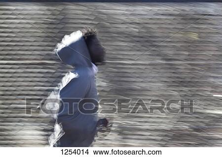 Picture - A young man jogging in front of a chain link fence. Fotosearch