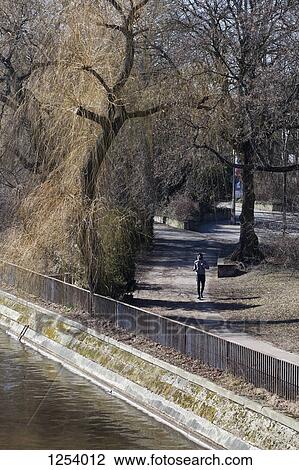 A young man jogging through a city park View Large Photo Image Stock Image - A young man jogging through a city park. Fotosearch