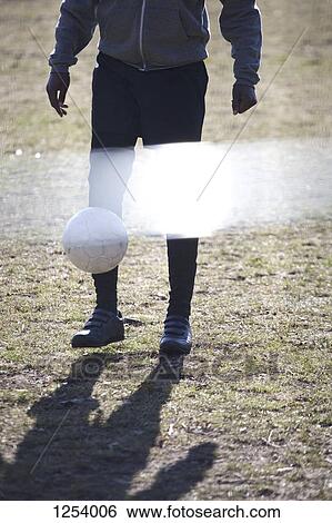 Stock Photograph - A young man kicking a soccer ball in a park. Fotosearch