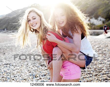 A young woman giving her teenage friend a piggyback ride at the beach View Large Photo Image Stock Photograph - A young woman giving her teenage friend a piggyback ride at the beach. Fotosearch