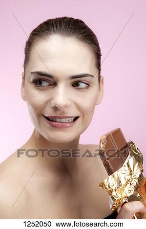 Stock Image - A young woman holding a large chocolate bar looking guilty. Fotosearch