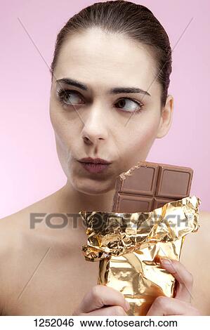 A young woman holding a large chocolate bar looking guilty View Large Photo Image Stock Photograph - A young woman holding a large chocolate bar looking guilty. Fotosearch