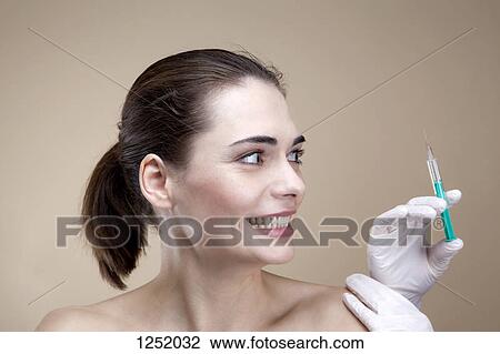 Stock Image - A young woman looking anxiously at a hands holding a syringe. Fotosearch