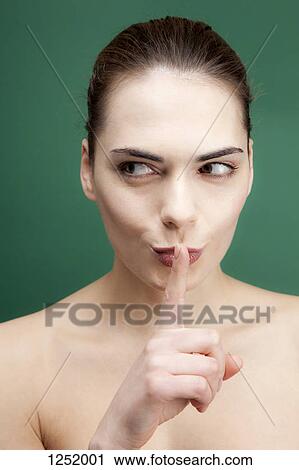 A young woman looking to the side while putting her finger to her lips playfully View Large Photo Image Stock Image - A young woman looking to the side while putting her finger to her lips playfully. Fotosearch