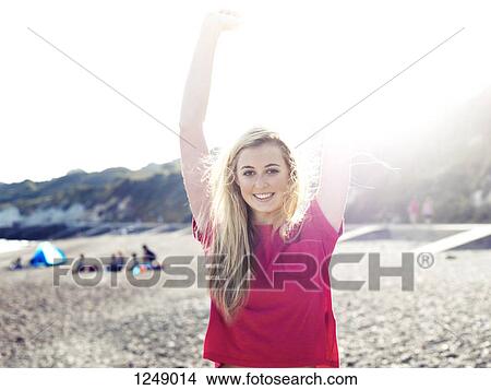 Picture - A young woman stretching in the sunlight on a beach. Fotosearch
