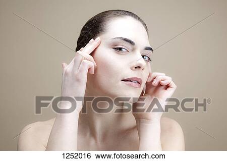 A young woman with her fingers on her temples pulling the skin back View Large Photo Image Stock Photograph - A young woman with her fingers on her temples pulling the skin back. Fotosearch
