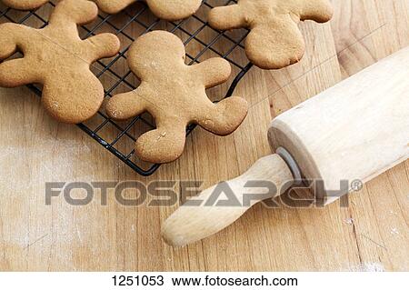 Stock Image - Gingerbread man cookies cooling on a rack next to a rolling pin. Fotosearch