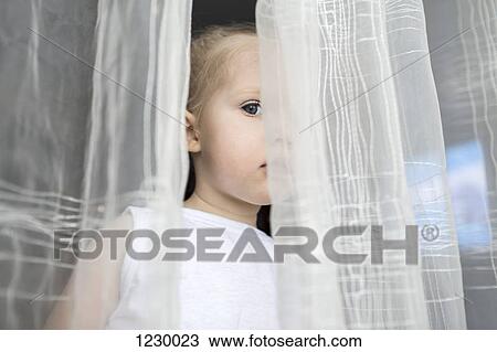 Stock Image - Girl peeking between translucent curtains. Fotosearch