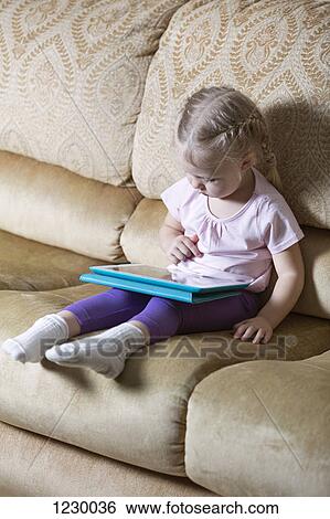 Girl using digital tablet on sofa View Large Photo Image Stock Photograph - Girl using digital tablet on sofa. Fotosearch