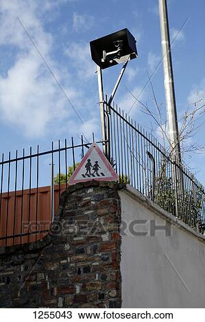 Stock Image - Low angle view of a video surveillance camera attached to a fence. Fotosearch