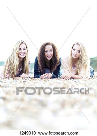 Stock Image - Three cheerfully smiling friends lying on a rocky beach. Fotosearch